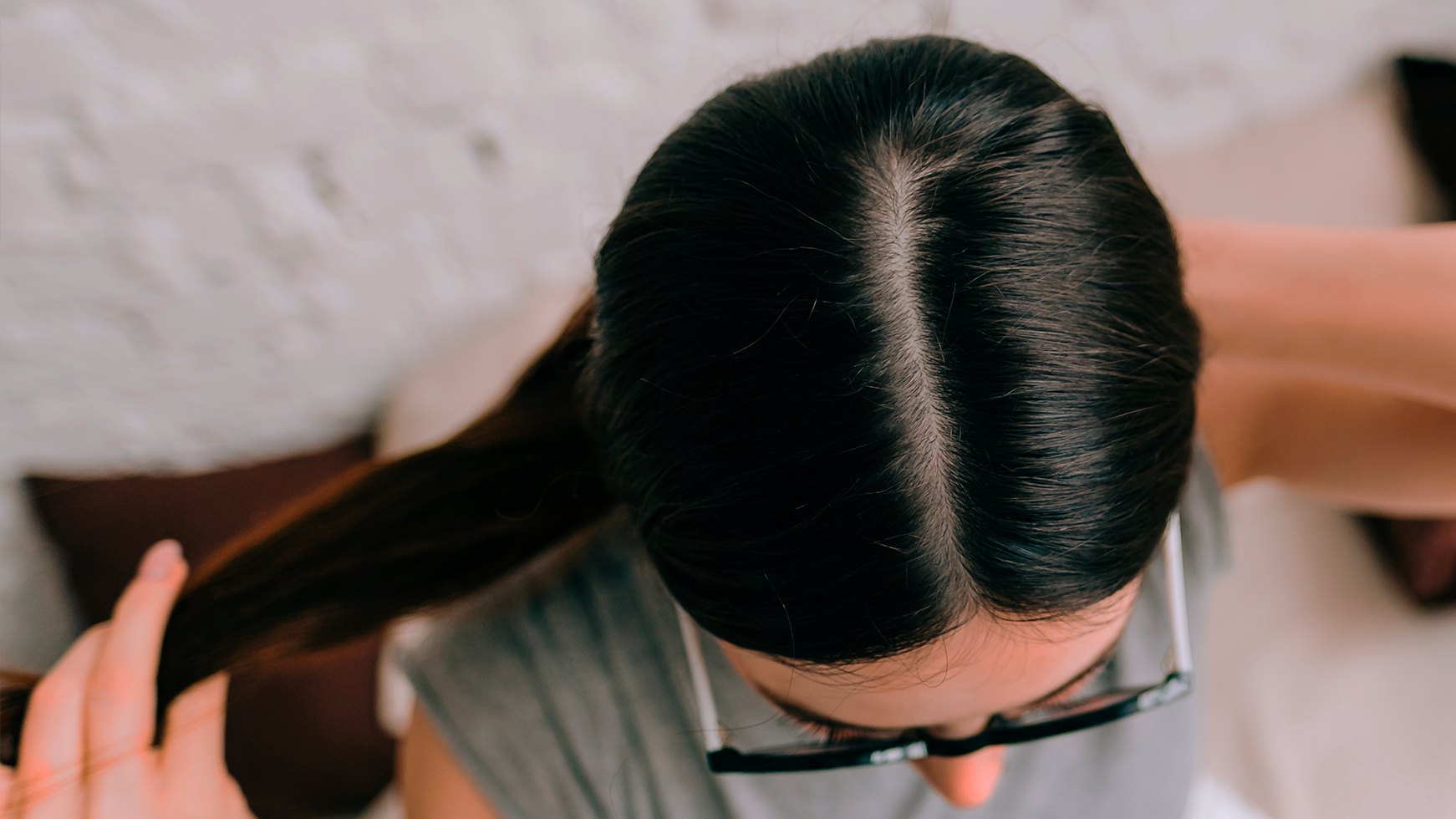 Topo da cabeça de mulher com cabelo escuro mostrando risca central e couro cabeludo, vista superior