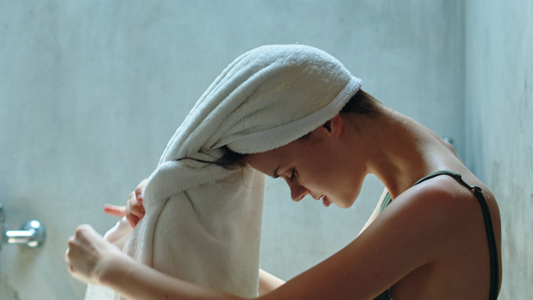 Mulher jovem secando o cabelo com toalha branca no banheiro após o banho, vista de perfil